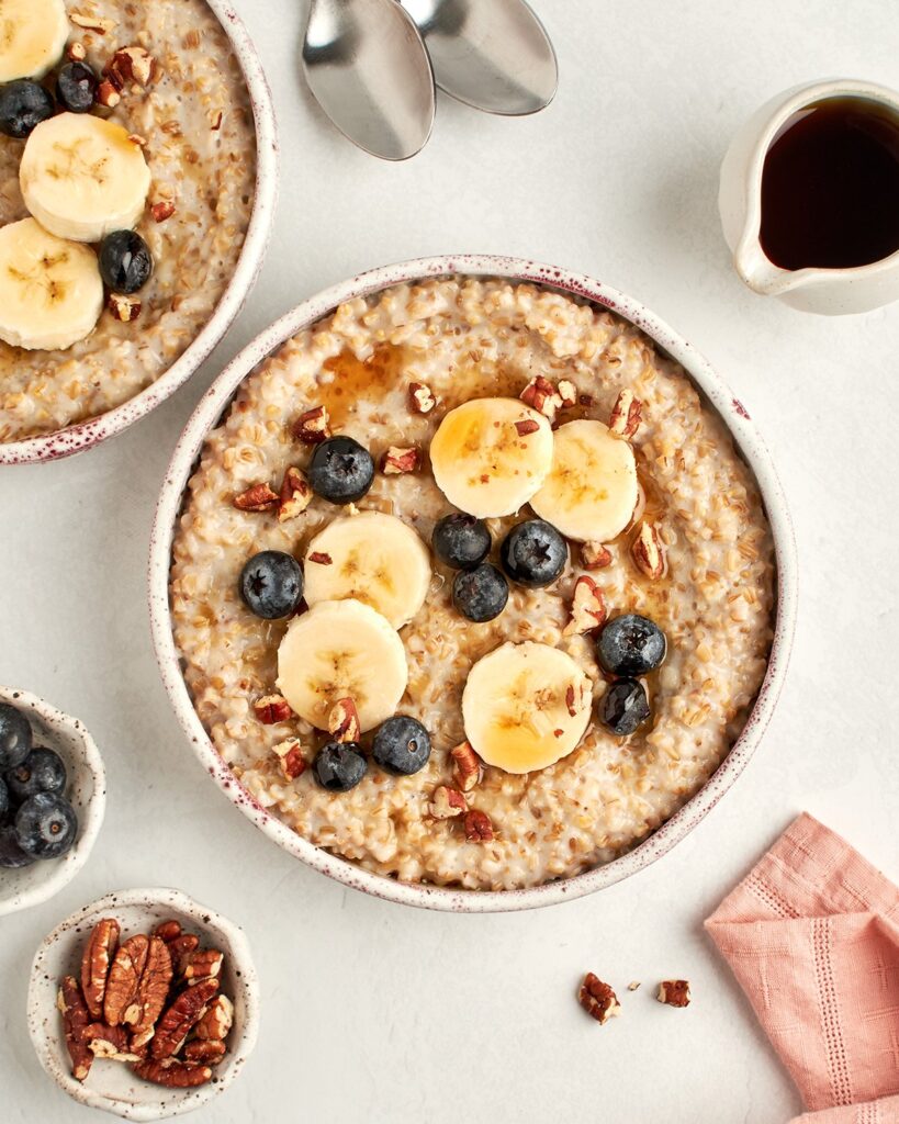 bowls of steel cut oats topped with blueberries, bananas, pecans and maple syrup