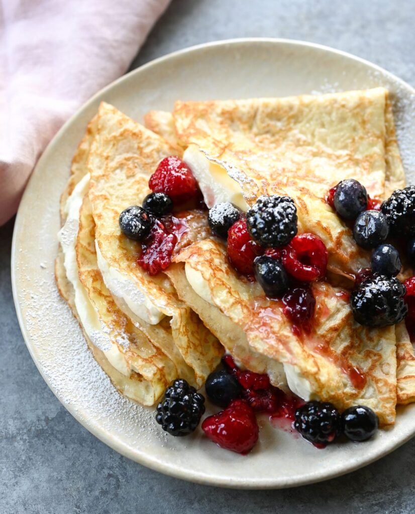 crepes on plate with cream and berries.