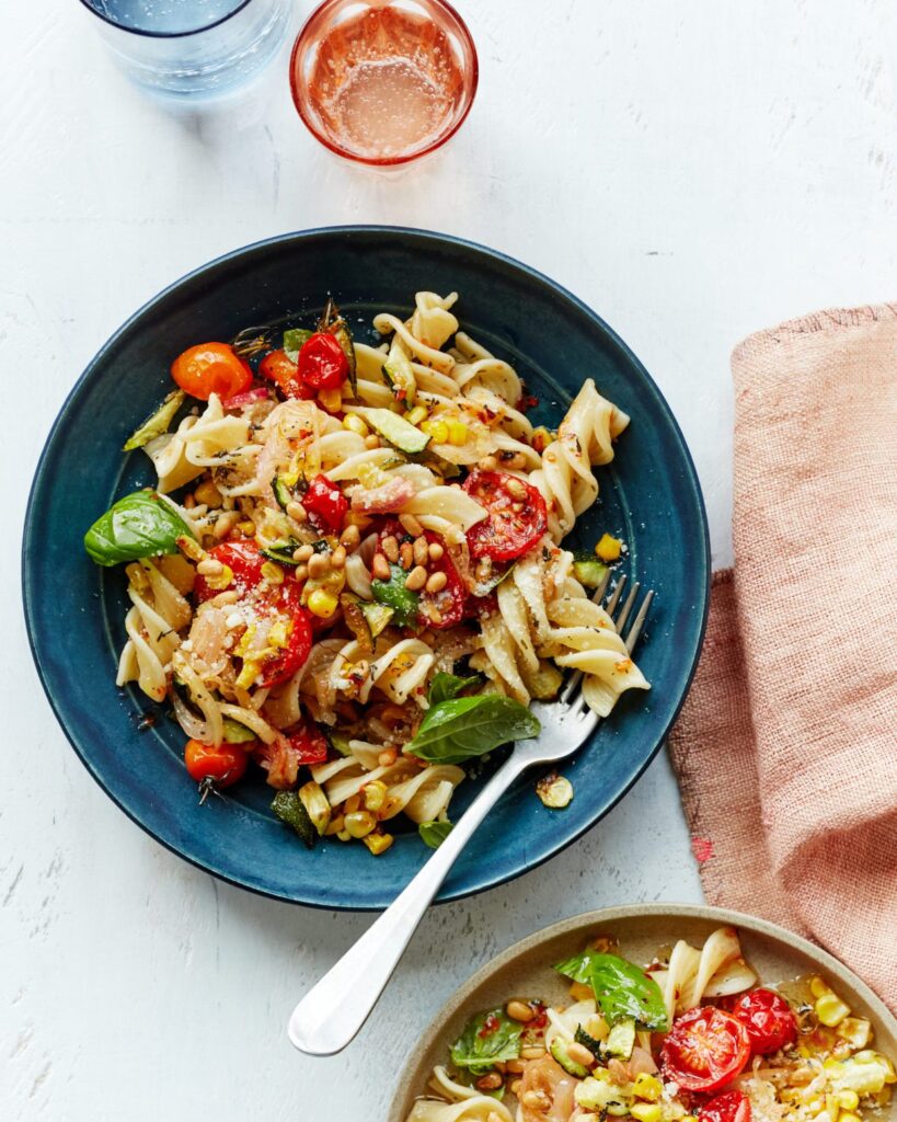 Summer pasta primavera on a blue plate with a fork.